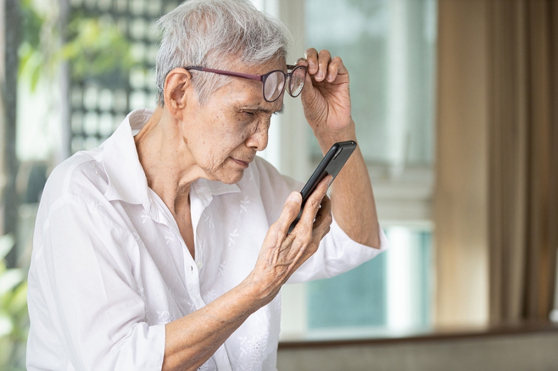 An elderly woman with cataracts struggling to read her phone